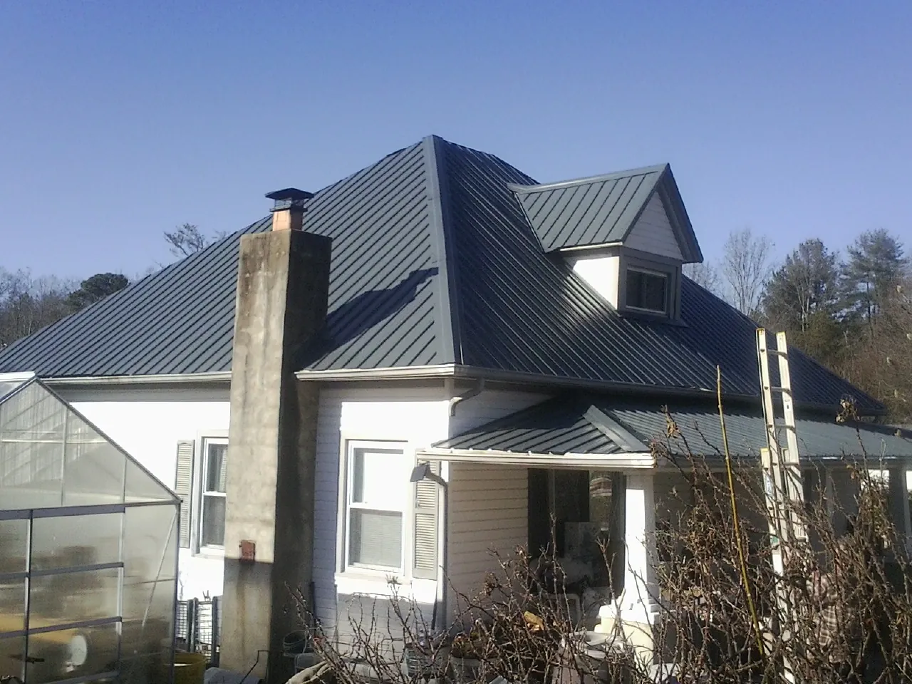 Dark blue standing seam metal roof on a white farmhouse with dormer in Strasburg