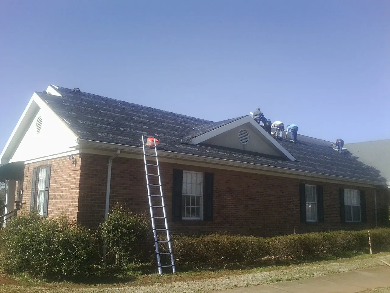 Crew tearing shingles off a brick ranch roof with a ladder set — Emergency Roof Repair work by our crew in Strasburg