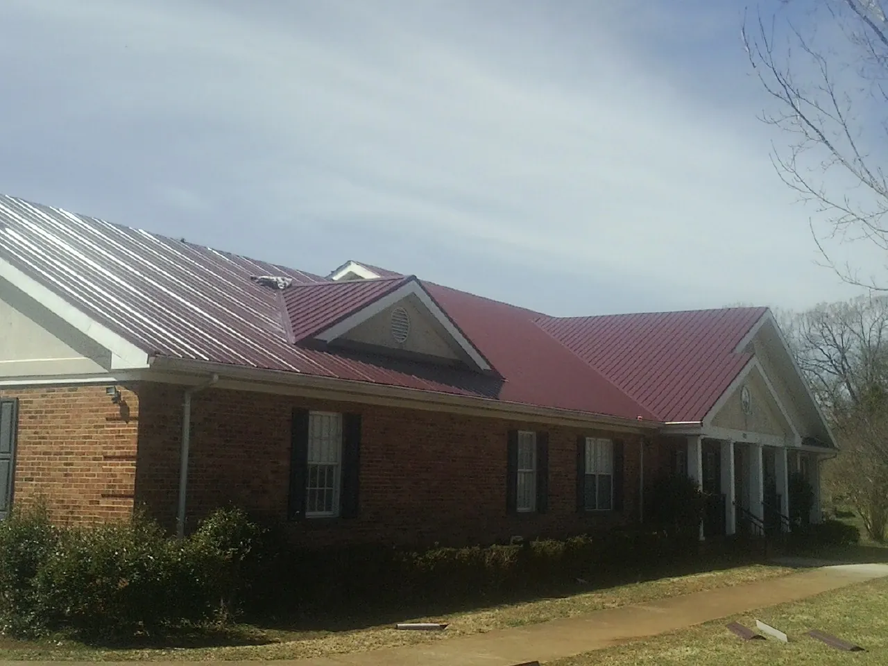 Red metal roof with gabled entries on a long brick building, from a Hail Damage Roof Repair job in Strasburg